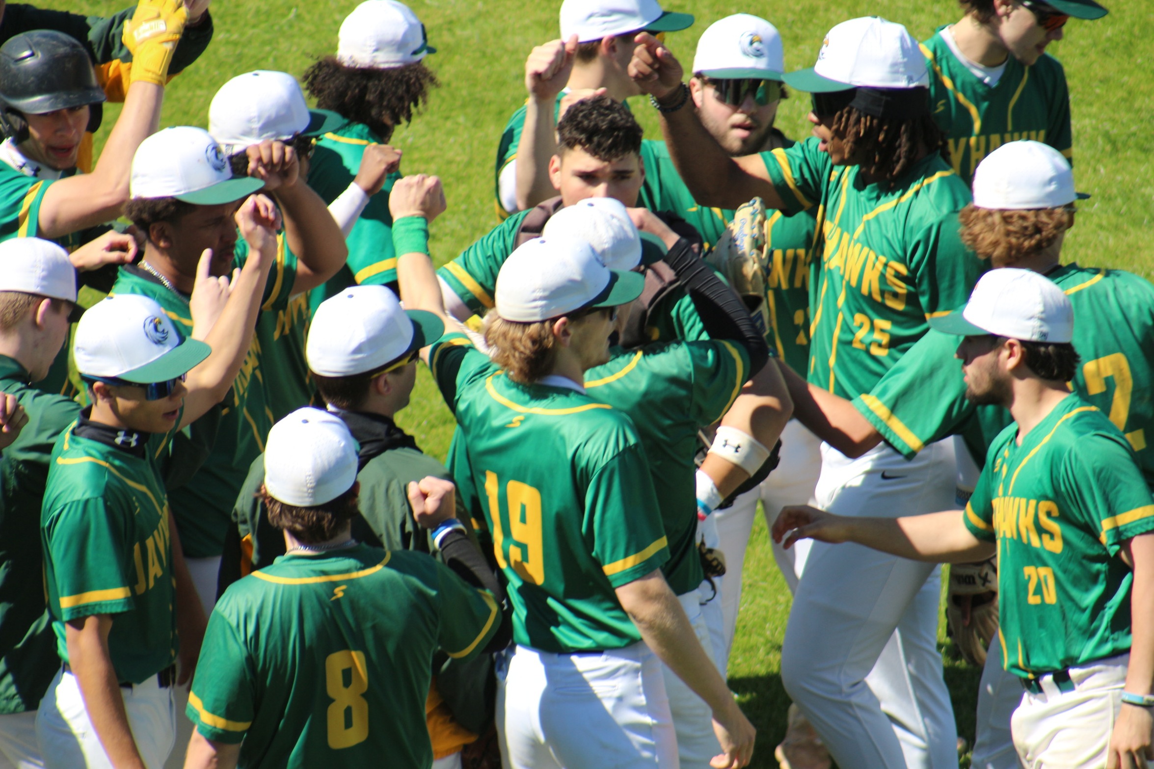 Photo of JCC baseball huddled up in their green jerseys.